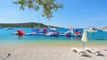 Ein Strand mit klarem Wasser, Booten und aufblasbaren Spielgeräten.