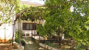 A garden pathway leading to a building with a pergola, surrounded by greenery and a small table. - Apartment Anton (Slatine)