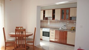 A kitchen with wooden cabinets, a white stove, and a dining table with chairs. - Apartment Anton (Slatine)