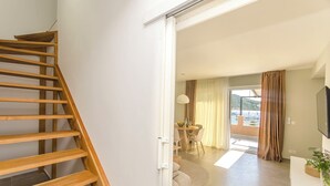 A modern interior with a wooden staircase, a dining area with a table and chairs, and a view through a large window. - Apartment Danijela (Primosten)