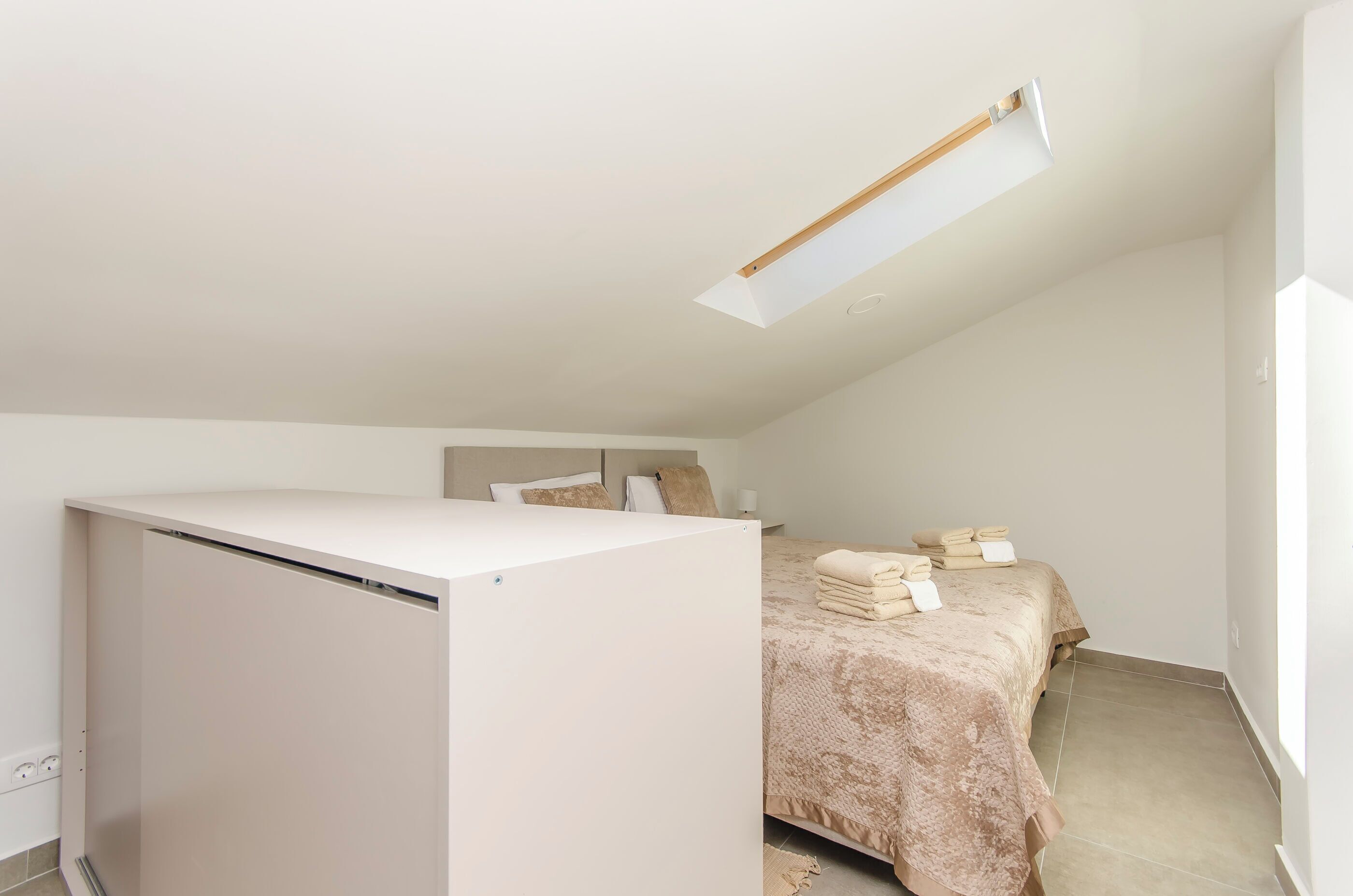 A small, modern bedroom with a bed, a desk, and a skylight.