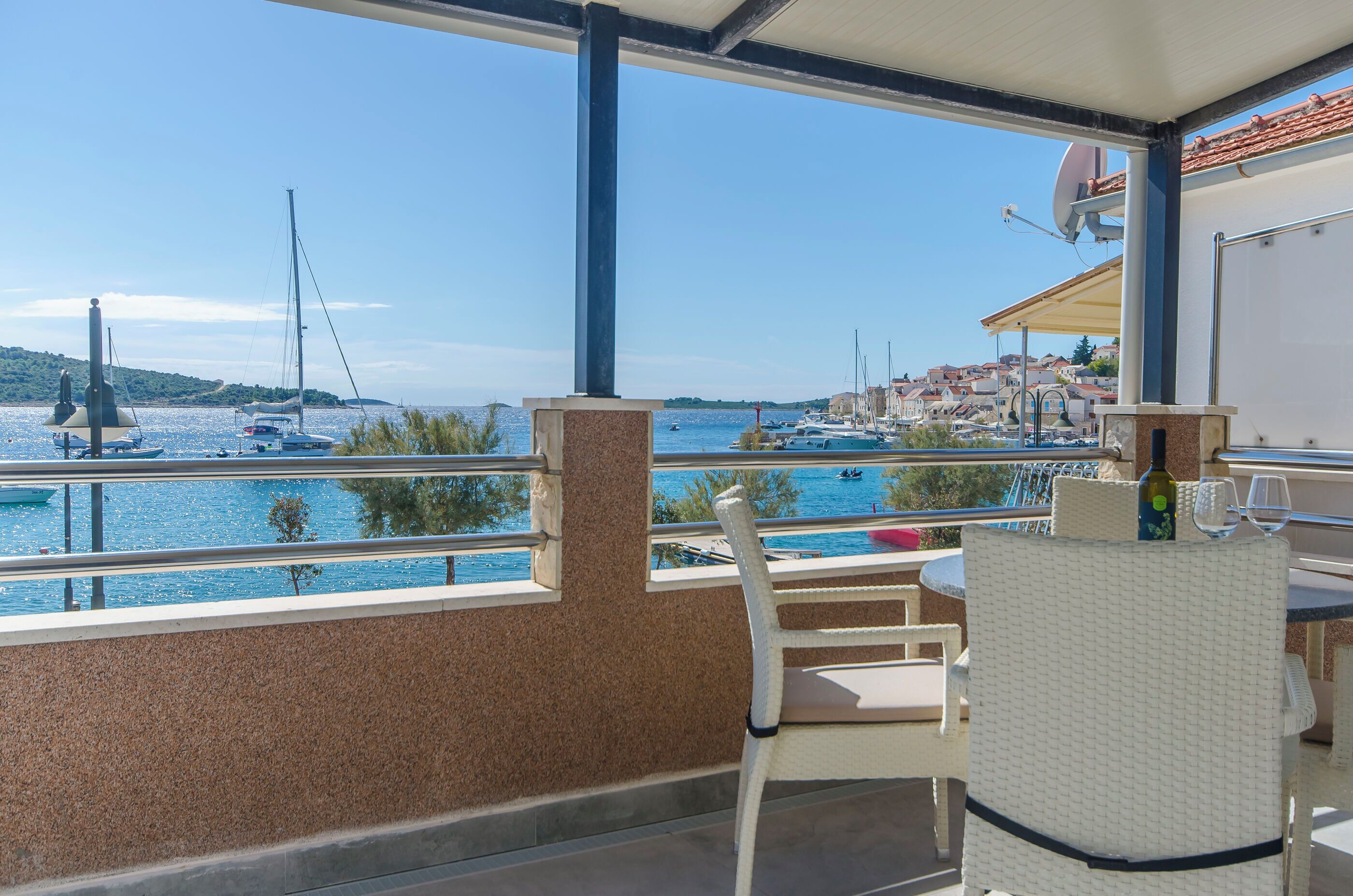 A balcony with a view of the sea, a table with a bottle and glass, and a chair.
