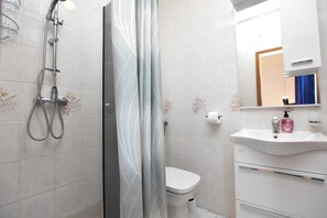 Un baño con ducha, inodoro, lavamanos y espejo.