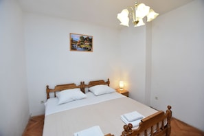 A bedroom with a wooden bed, white bedding, a nightstand with a lamp, and a painting on the wall. - Apartments Dusan (Primosten)