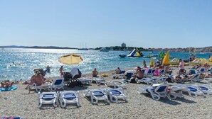 A beach with sun loungers and umbrellas, a water slide, and people swimming. - Apartment Niko (Vodice)