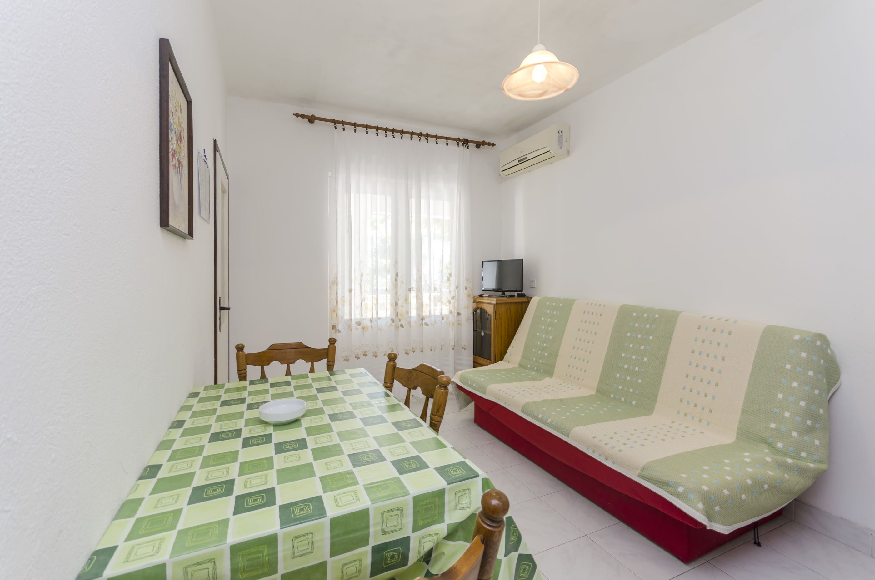 A room with a dining table, chairs, a sofa, a television, and a window with curtains.