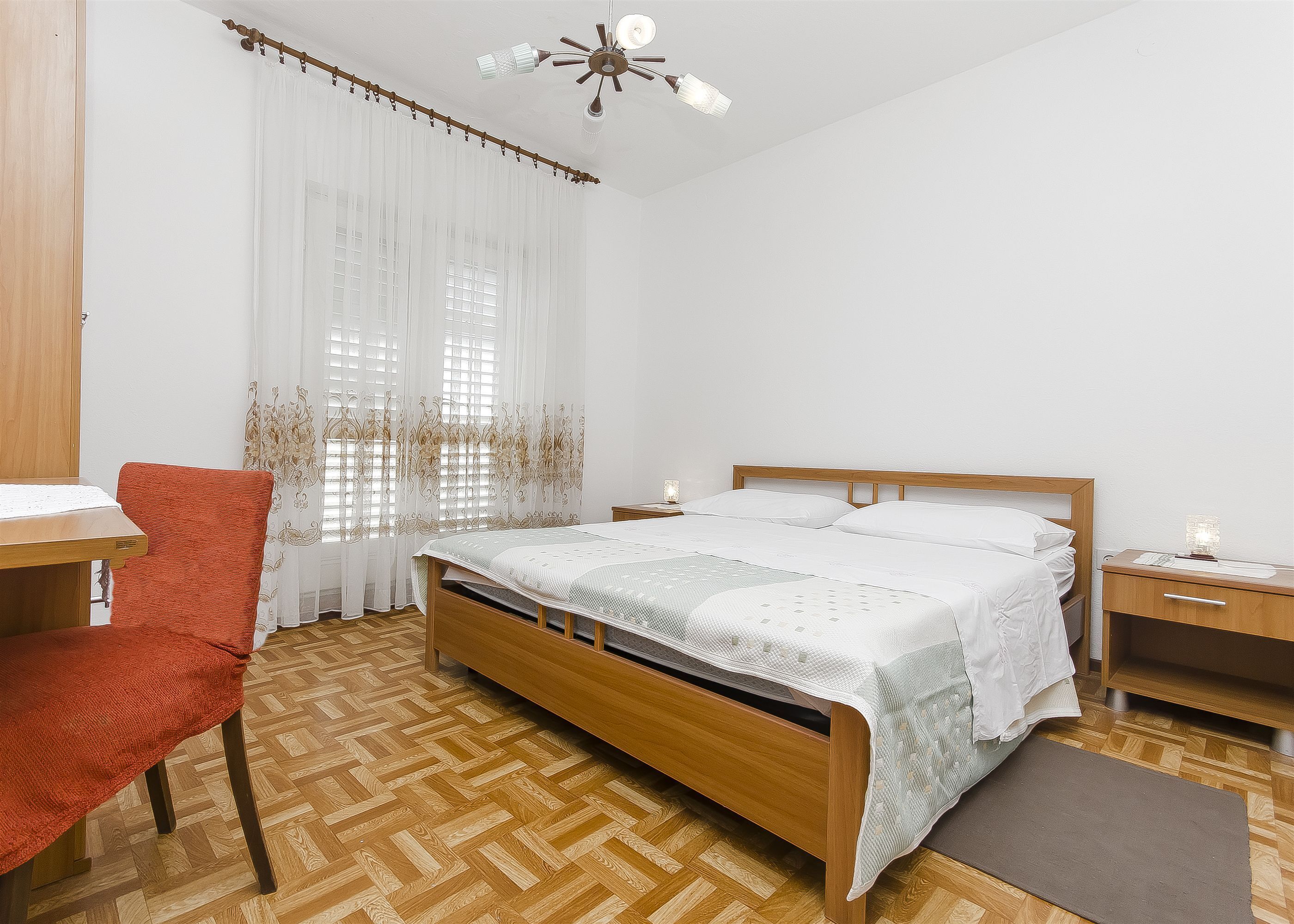 A bedroom with a wooden bed, a chair, a bedside table, and a nightstand.