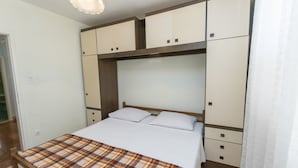 A bedroom with a bed, a plaid blanket, a wooden headboard, and built-in cabinets. - Apartment Smiljan (Primosten)