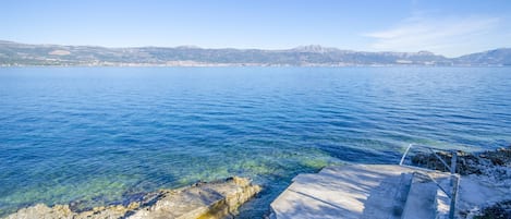 Vista costera con agua cristalina, costa rocosa y montañas al fondo.