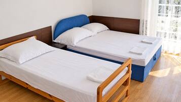 Una habitación con dos camas individuales, cabeceros de madera, ropa de cama blanca y una ventana con cortinas.