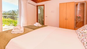A bedroom with a bed, a wooden wardrobe, and a balcony with a view of greenery. - Apartments and Room Milka-jere (Primosten)