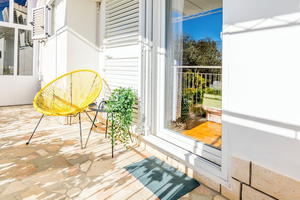 A patio with a yellow chair, a potted plant, and a glass door leading to a balcony.