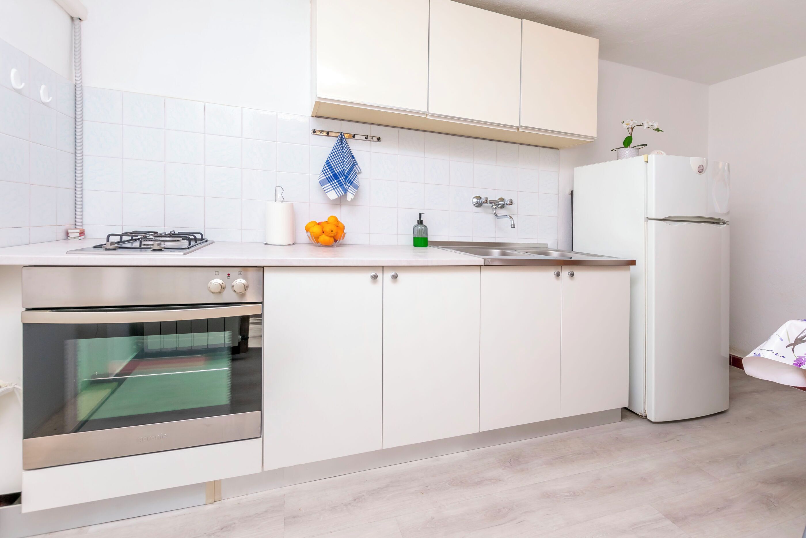 A modern kitchen with white cabinets, a gas stove, an oven, a sink, and a refrigerator.