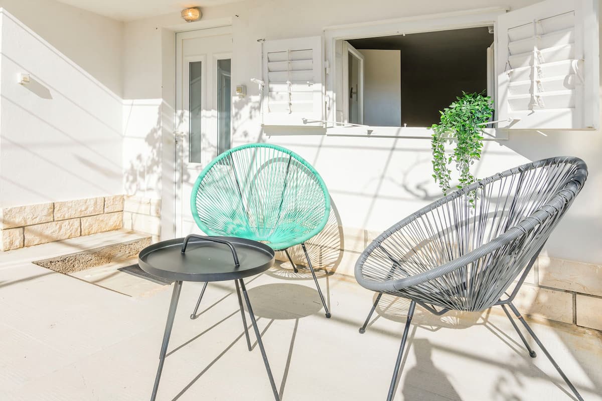 An outdoor seating area with two chairs and a table, a potted plant, and a door leading to a covered entrance.