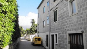 Une rue étroite où est garé un fourgon jaune sur le bord, bordée d’immeubles en pierre dotés de nombreuses fenêtres et portes.