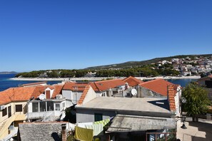 A coastal town with terracotta-roofed buildings, a beach in the background, and a clear blue sky.