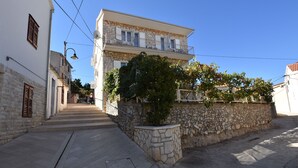 A two-story building with a stone facade, a balcony with railings, and a small garden area. - Apartments Zdenka (Primosten)