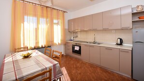 A kitchen with a dining table, chairs, a stove, and cabinets. - Apartments Zdenka (Primosten)