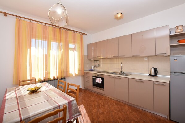 A kitchen with a dining table, chairs, a stove, and cabinets. - Apartments Zdenka (Primosten)