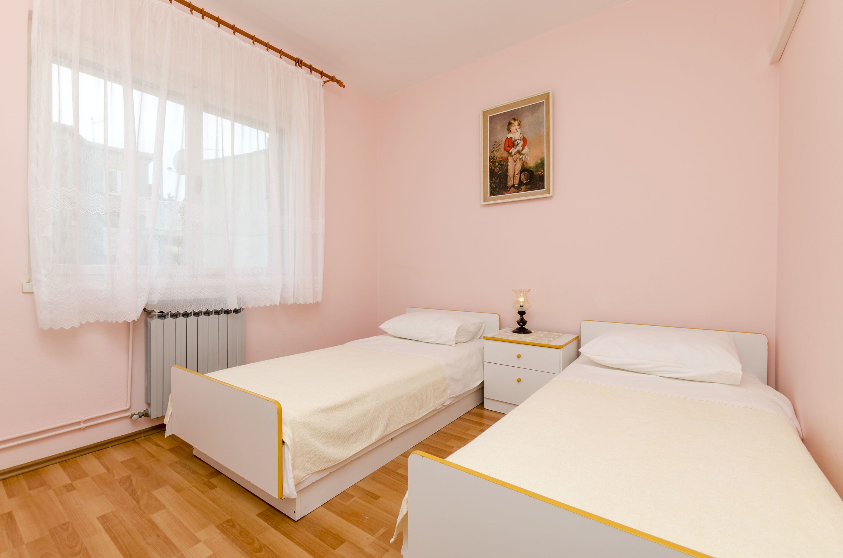 A bedroom with two single beds, a nightstand with a lamp, and a radiator.