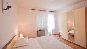A bedroom with a bed, bedside lamp, wardrobe, and a window with sheer curtains. - Apartments Zdenka (Primosten)