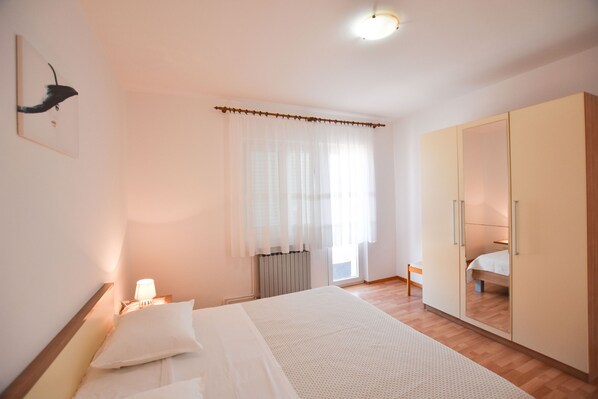 Une chambre à coucher comprenant un lit, une lampe de chevet, une armoire et une fenêtre avec des rideaux légers.
