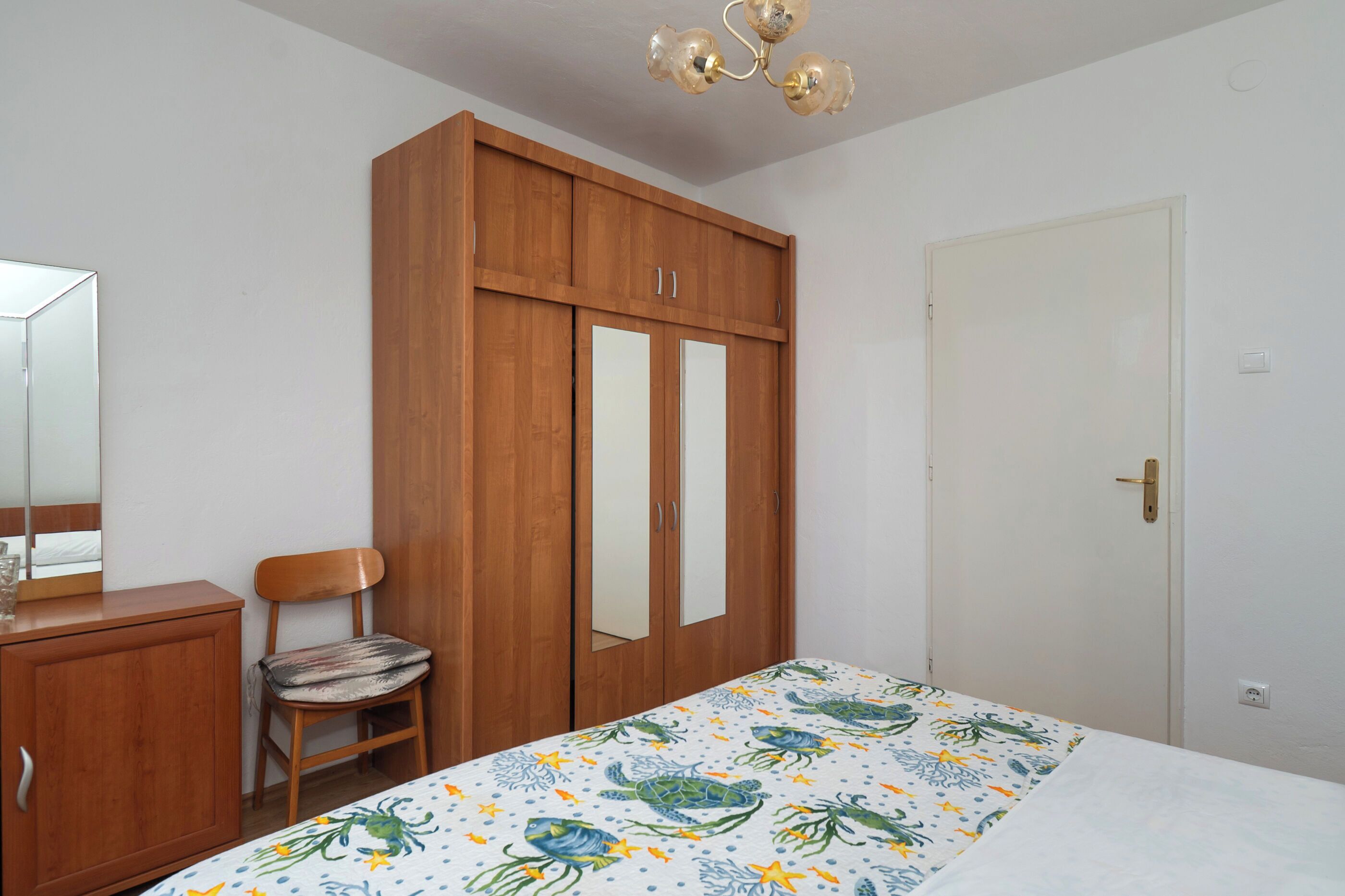A bedroom with a bed, wooden wardrobe, chair, and a door.
