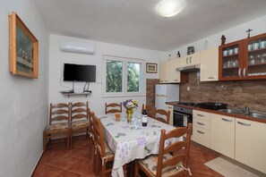 A kitchen with a dining table, chairs, a TV, and a window. - Apartment Marin (Primosten)