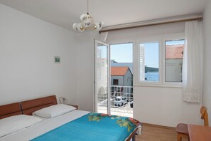 A bedroom with a bed, a chair, a balcony with a railing, and a view of buildings and water. - Apartment Marin (Primosten)