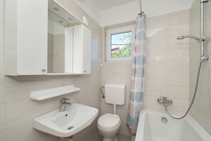 A bathroom with a sink, toilet, bathtub, and a window above the toilet. - Apartment Marin (Primosten)