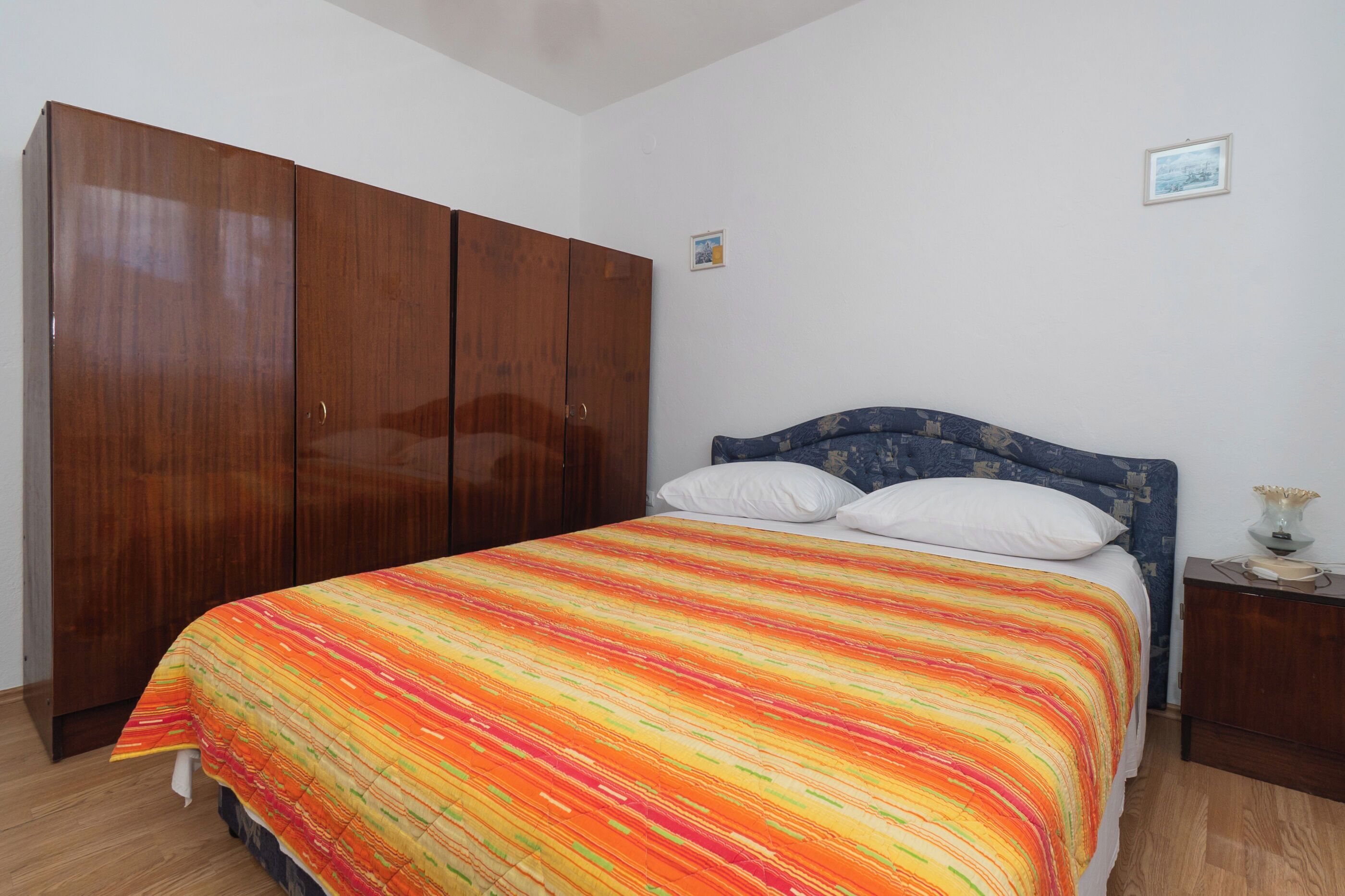 A bedroom with a bed, wooden wardrobe, and a nightstand.