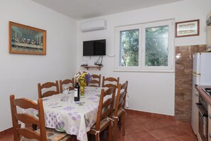 A dining area with a table set for four, a TV mounted on the wall, and a window with a view of trees. - Apartment Marin (Primosten)