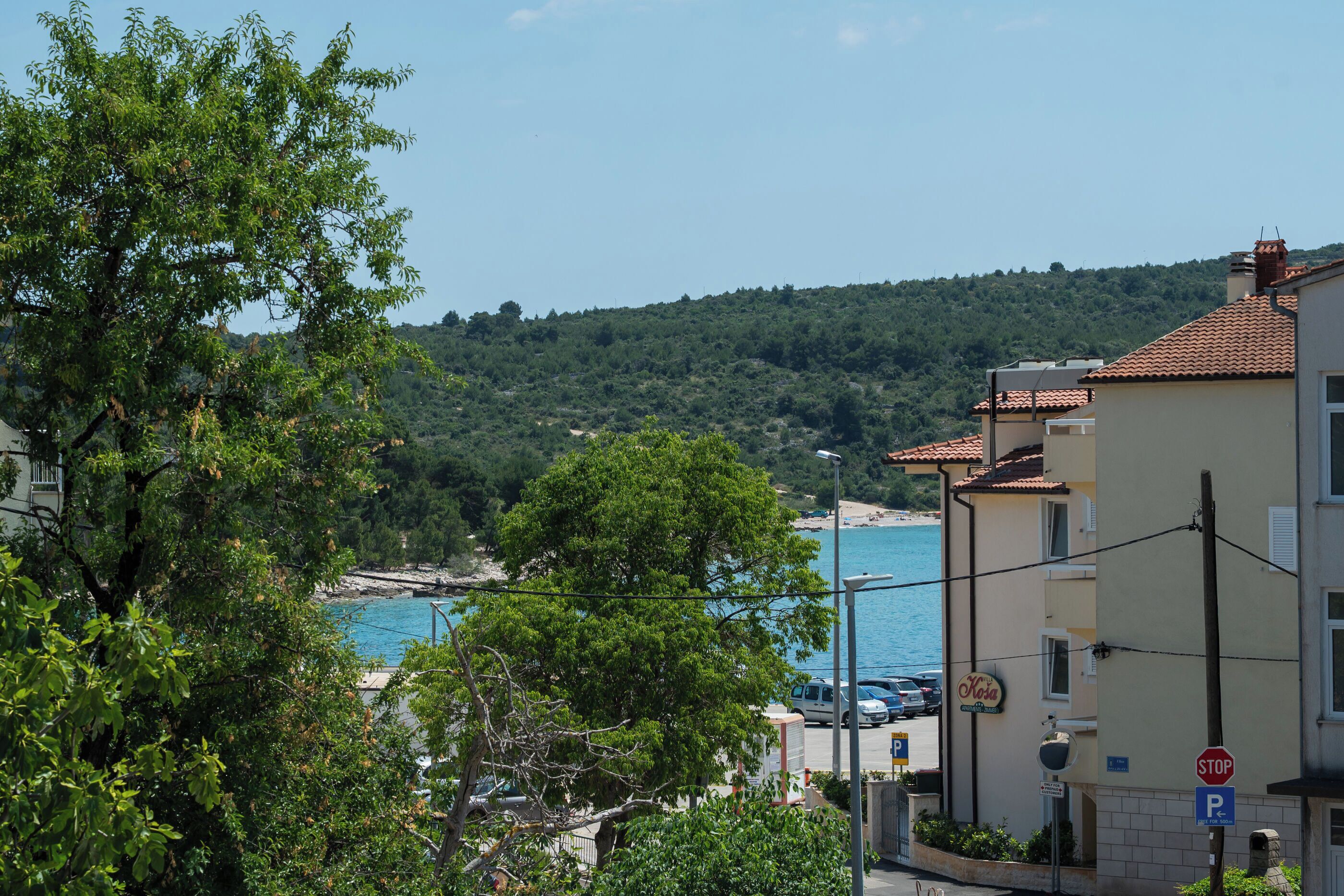 A coastal building with a stop sign, a parking sign, and a view of the sea and hills.