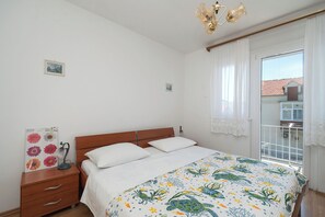 A bedroom with a bed, a nightstand, a lamp, and a window with curtains. - Apartment Marin (Primosten)