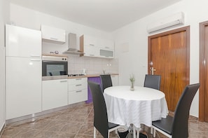 A compact kitchen with white cabinets, a stove, and a microwave. There's a dining table with chairs and a small plant on it.