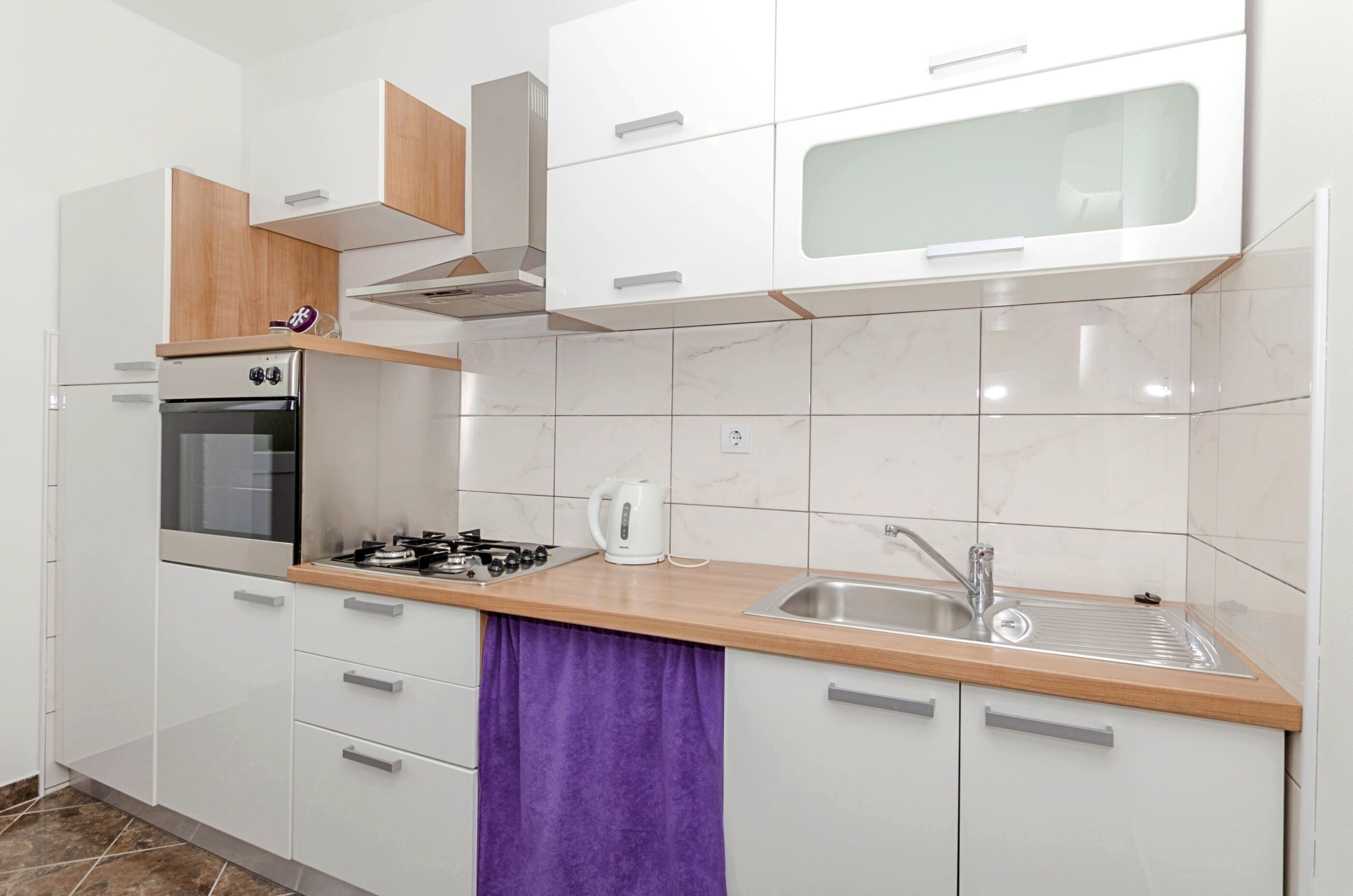 A modern kitchen with white cabinets, a stainless steel sink, a gas stove, and a built-in oven.