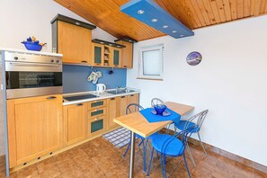 A compact kitchen with wooden cabinets, a built-in oven, a sink, and a dining area with blue chairs.