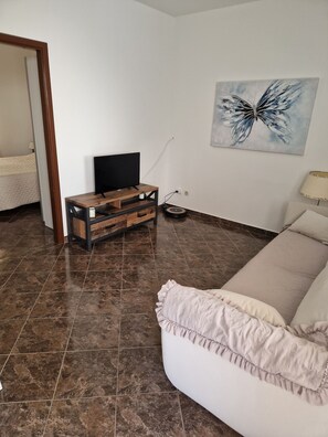 A modern living room with a flat-screen TV on a wooden stand, a painting on the wall, and a beige sofa.
