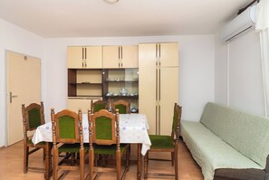 A dining area with a table set for four, surrounded by wooden chairs with green upholstery. There is a sofa against the wall and a cabinet with shelves above the table. - Apartment Davorka (Primosten)