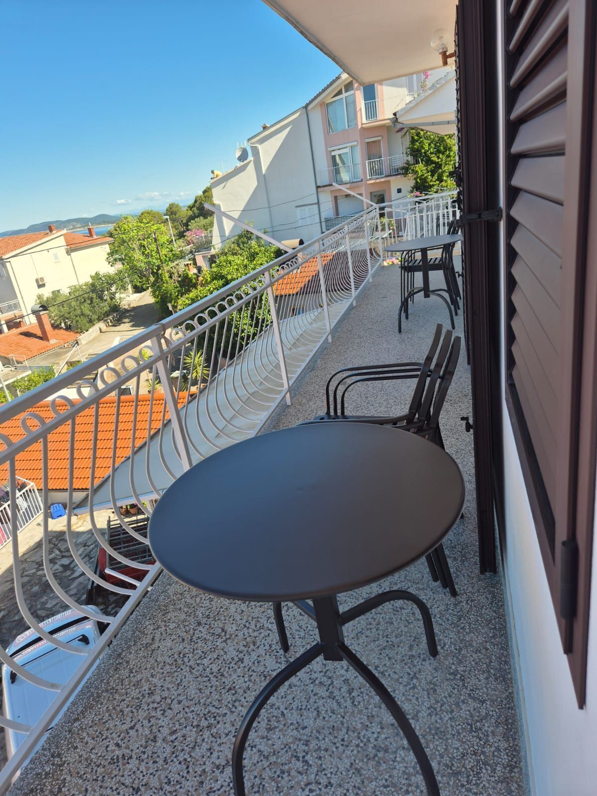 Un balcon avec une table ronde et deux chaises, donnant sur un quartier résidentiel avec des toits en tuiles et de la verdure.