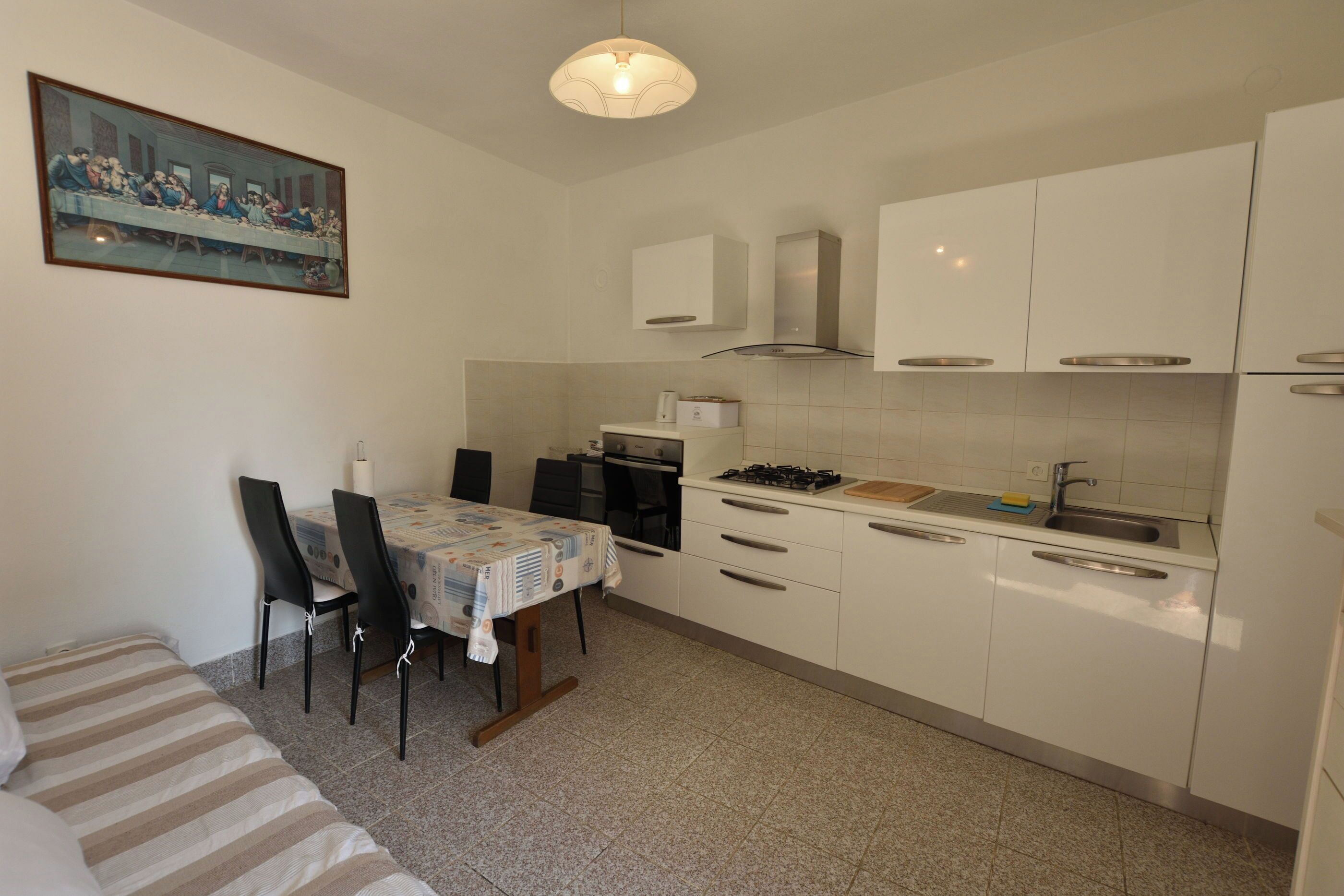 A compact kitchen with white cabinets, a dining table with chairs, and a painting on the wall.