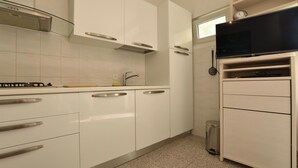 A modern kitchen with white cabinets, stainless steel handles, a microwave, and a trash bin. - Apartment Milka (Primosten)