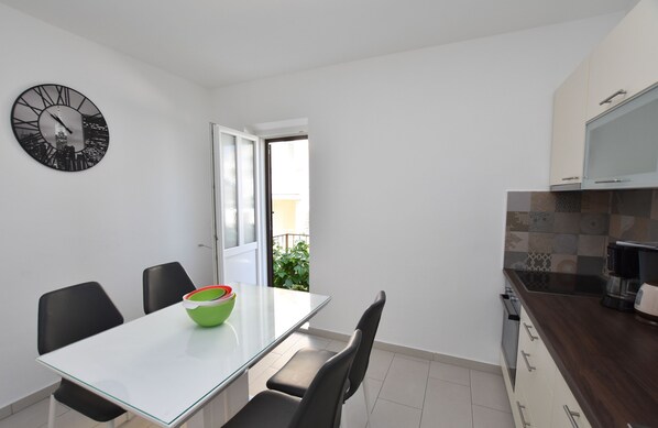 A modern kitchen with white cabinets, a dark countertop, and a green bowl on the table. - Apartments Guzela (Primosten)