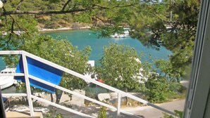 A view from a window overlooking a turquoise body of water with boats, trees, and a staircase leading down to a road. - Apartments Elvis (Primosten)