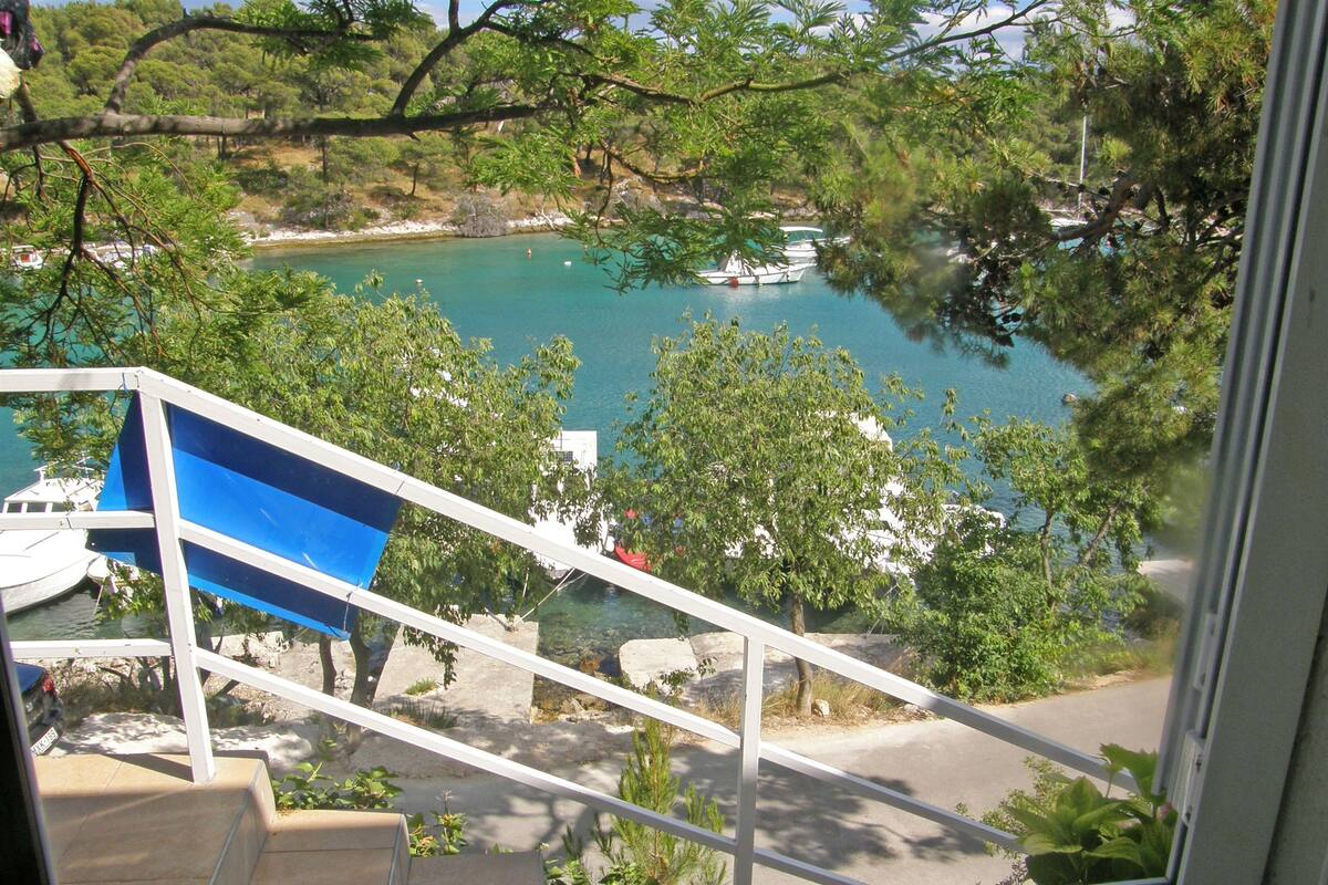 Vista desde una ventana sobre aguas turquesas con barcos, árboles y una escalera que baja a una carretera.