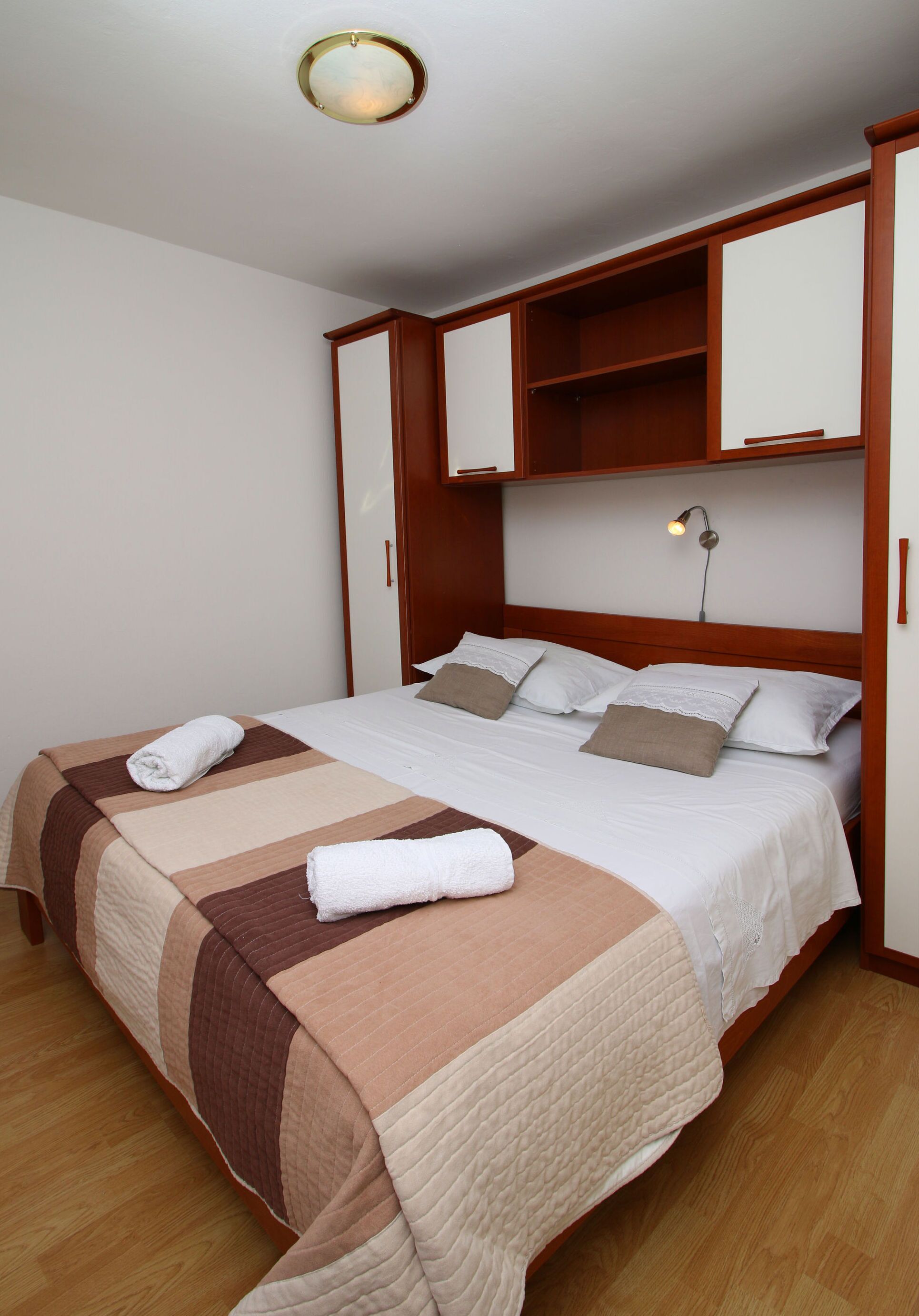 A neatly made bed with a striped blanket, a bedside lamp, and a wooden headboard.