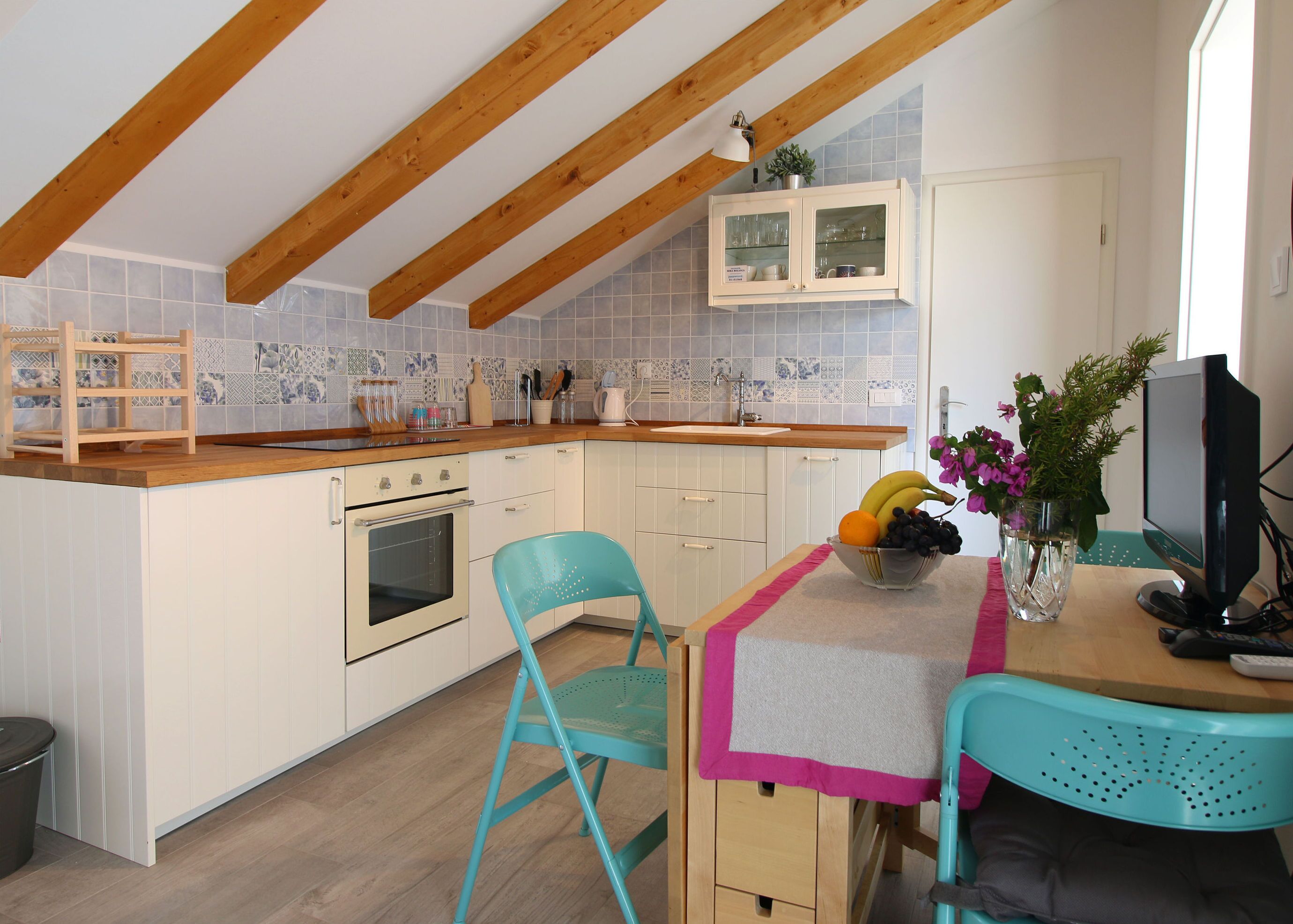 A kitchen with wooden beams, a tiled backsplash, a sink, a stove, and a dining area with chairs and a table.