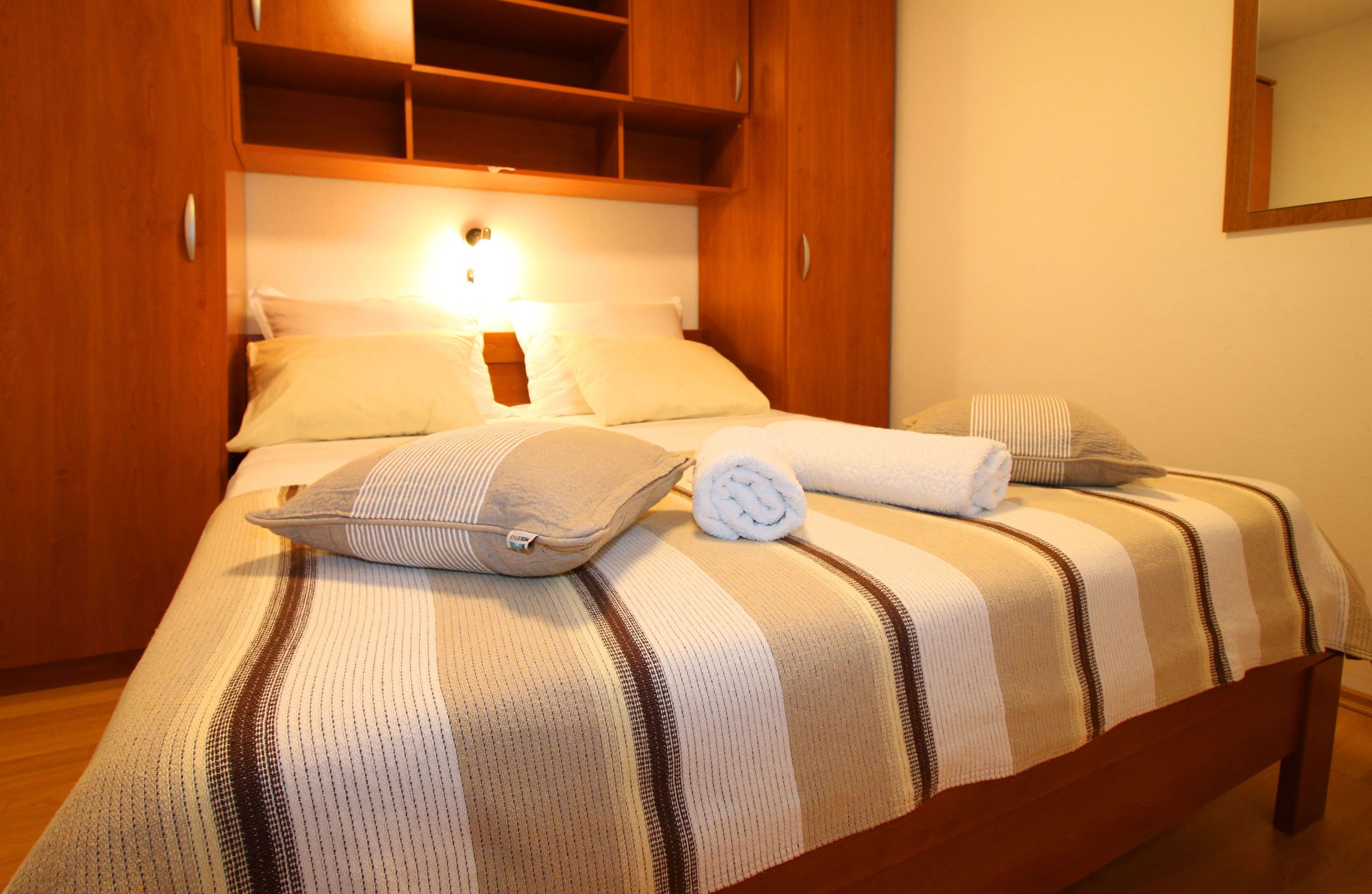 Cama bem arrumada com roupa de cama listrada, uma toalha enrolada e um travesseiro.