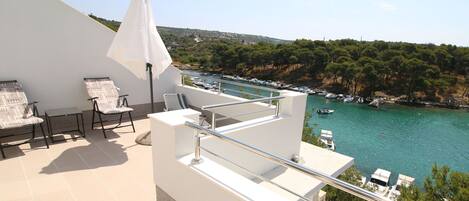 A balcony with outdoor furniture, a white umbrella, and a view of a marina with boats.