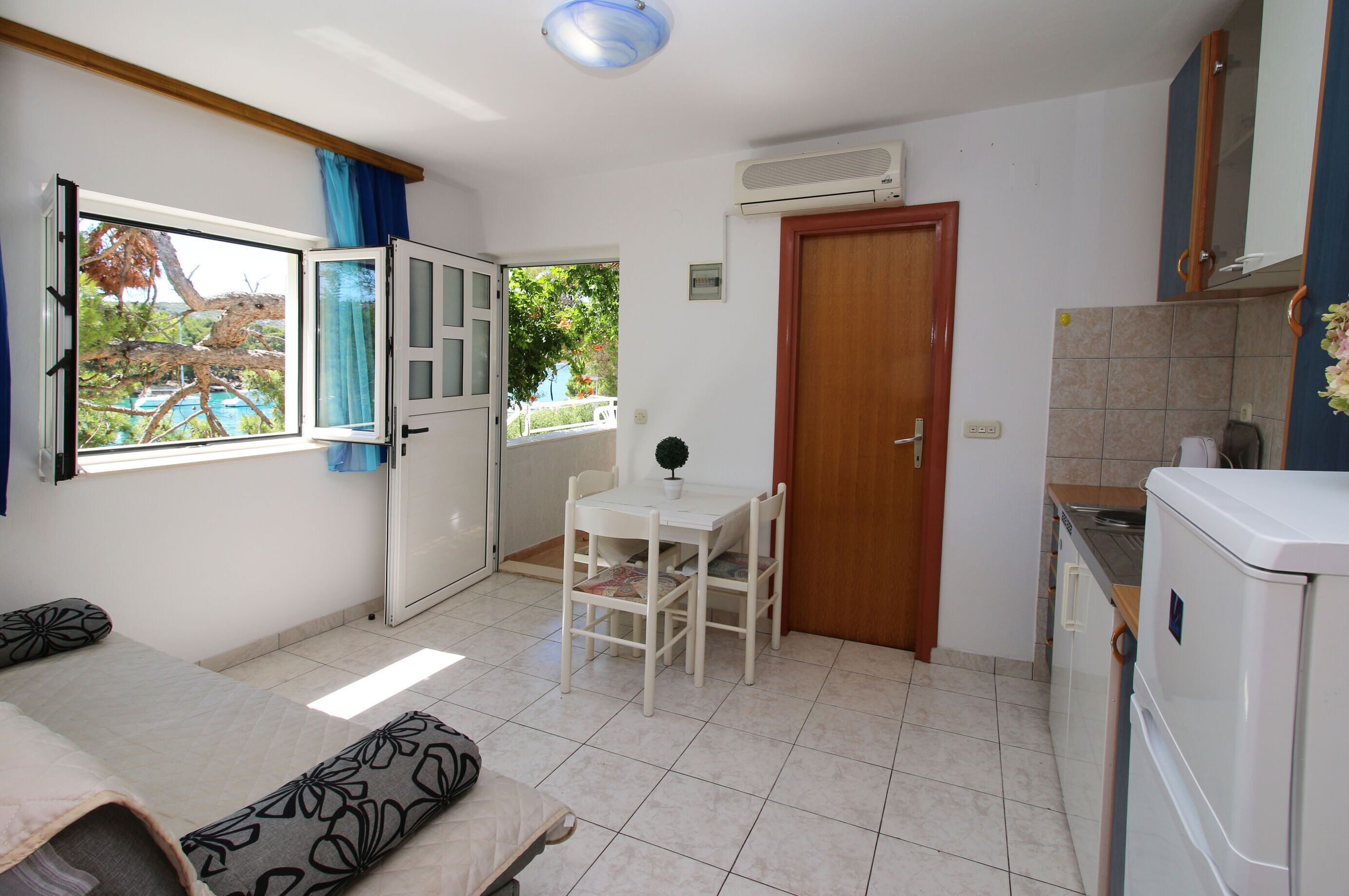 A compact kitchen with a dining area, a refrigerator, and a window with a view of greenery.